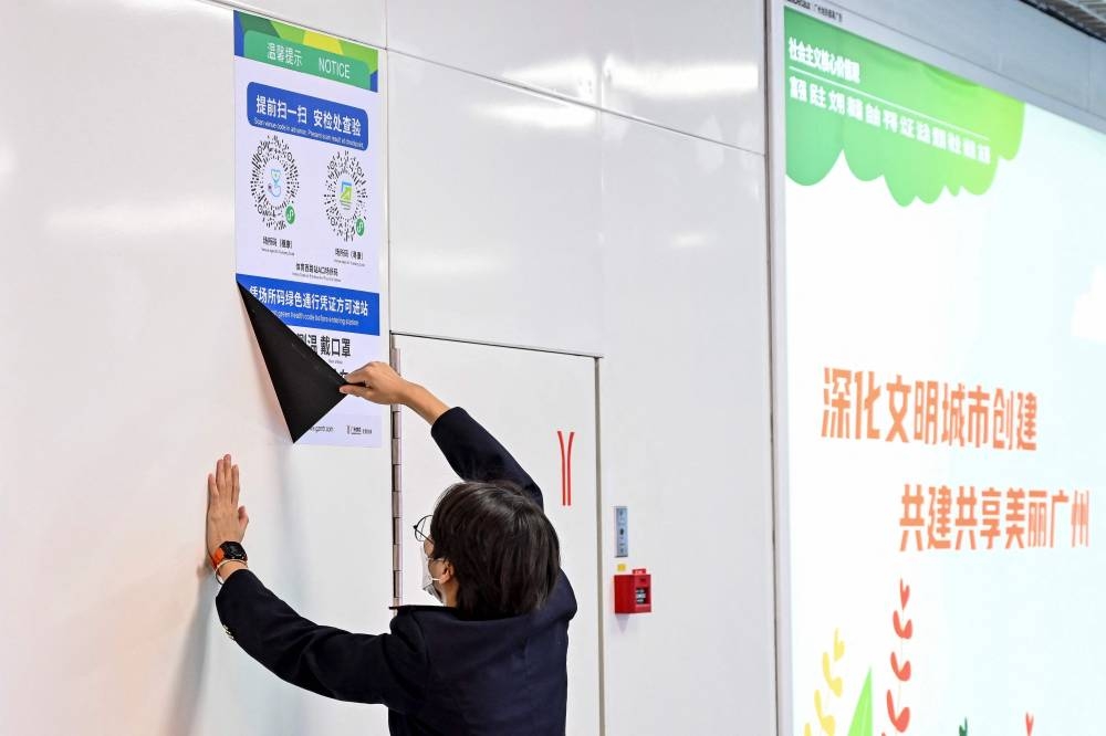 A subway staff member removes a poster for a Covid-19 health code used on entering the subway in Guangzhou December 7, 2022. ― Reuters pic