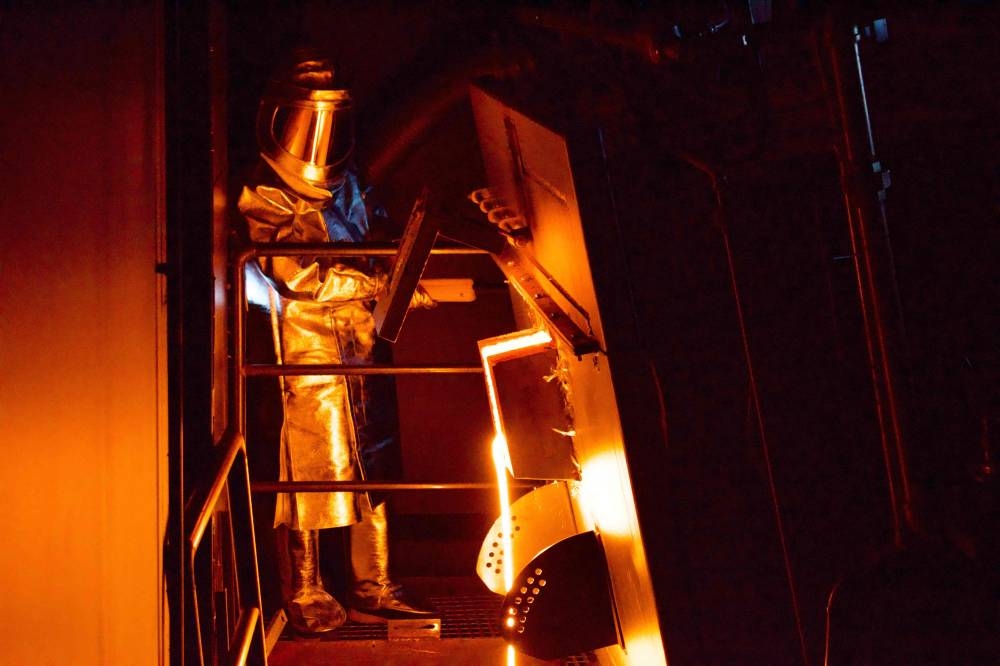A man in protective suit is seen as red molten lava pours from a furnace adjoining the showroom of the Lava Show in Reykjavik, Iceland, on December 1, 2022. — AFP pic