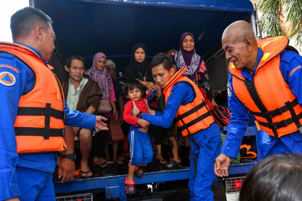  Kelantan Civil Defence Force (APM) personnel are seen helping flood victims from Kampung Serongga evacuate to a temporary relief centre in Pasir Mas December 12, 2022. — Bernama pic