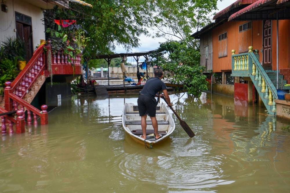 A flood victim is seen paddling a boat in Rantau Panjang, Pasir Mas December 12, 2022. — Bernama pic