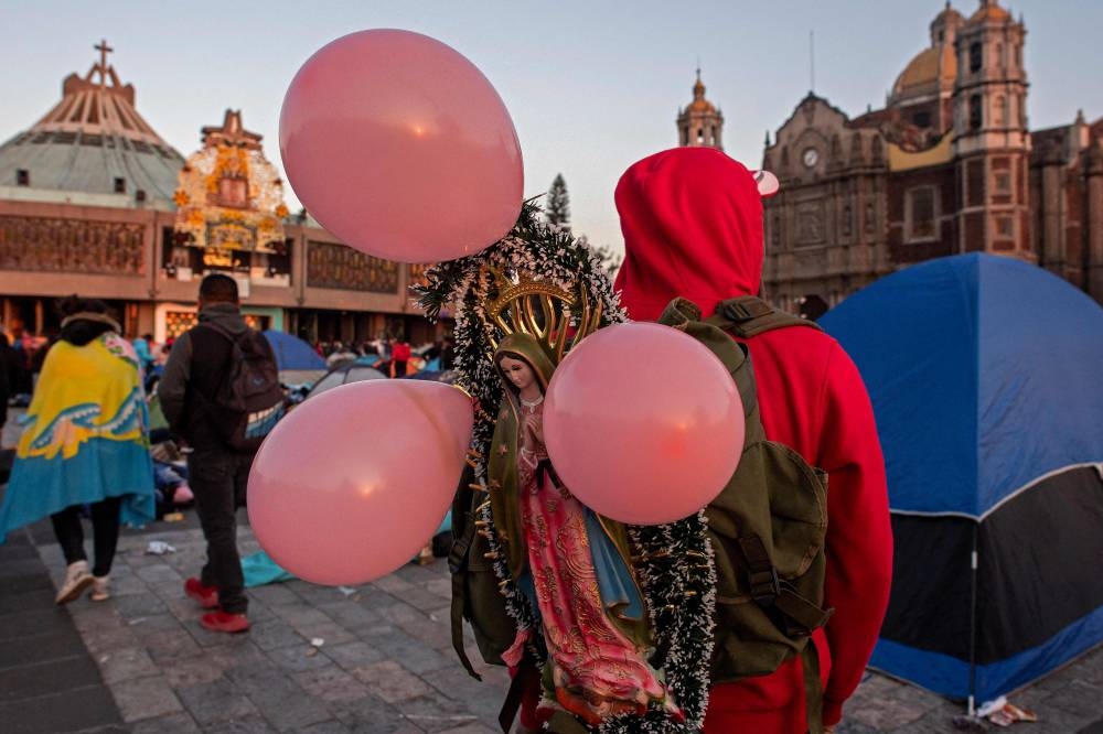 A pilgrim carries an image of the Virgin of Guadalupe with pink balloons outside the Basilica of Guadalupe in Mexico City on December 12, 2022. — AFP pic
