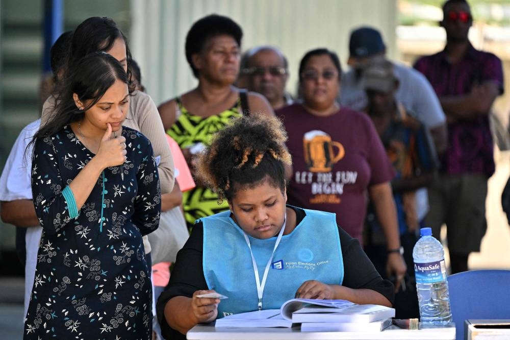 A staff checks the names on the voters list during the general elections at a polling station in Fiji capital city Suva on December 14, 2022. — AFP pic 