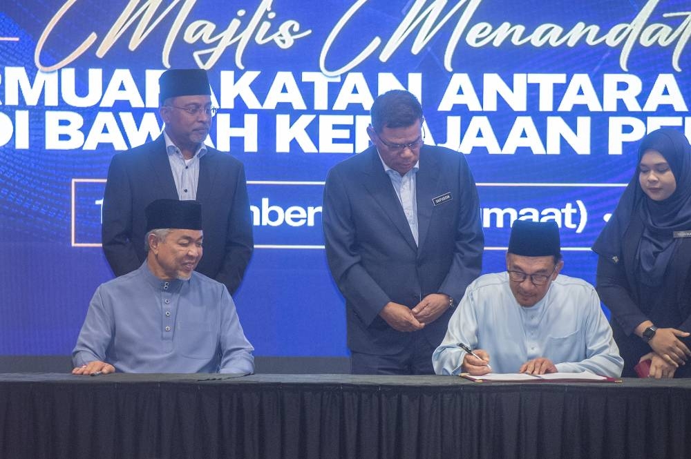Datuk Seri Dr Ahmad Zahid Hamidi looking on as Pakatan Harapan president, Datuk Seri Anwar Ibrahim signs the document during the National Unity government agreement signing ceremony at Perdana Putra in Putrajaya, December 16, 2022. — Picture by Shafwan Zaidon