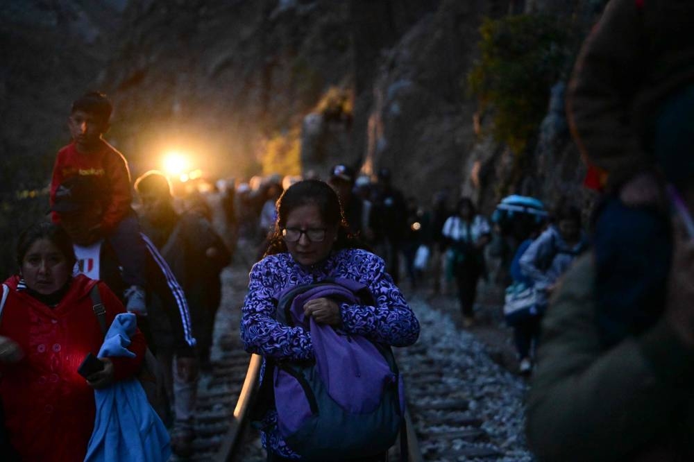 Stranded tourists who were visiting the Inca citadel of Machu Picchu walk along the railway track after being evacuated by train to Ollantaytambo, Peru, on December 17, 2022. — AFP pic