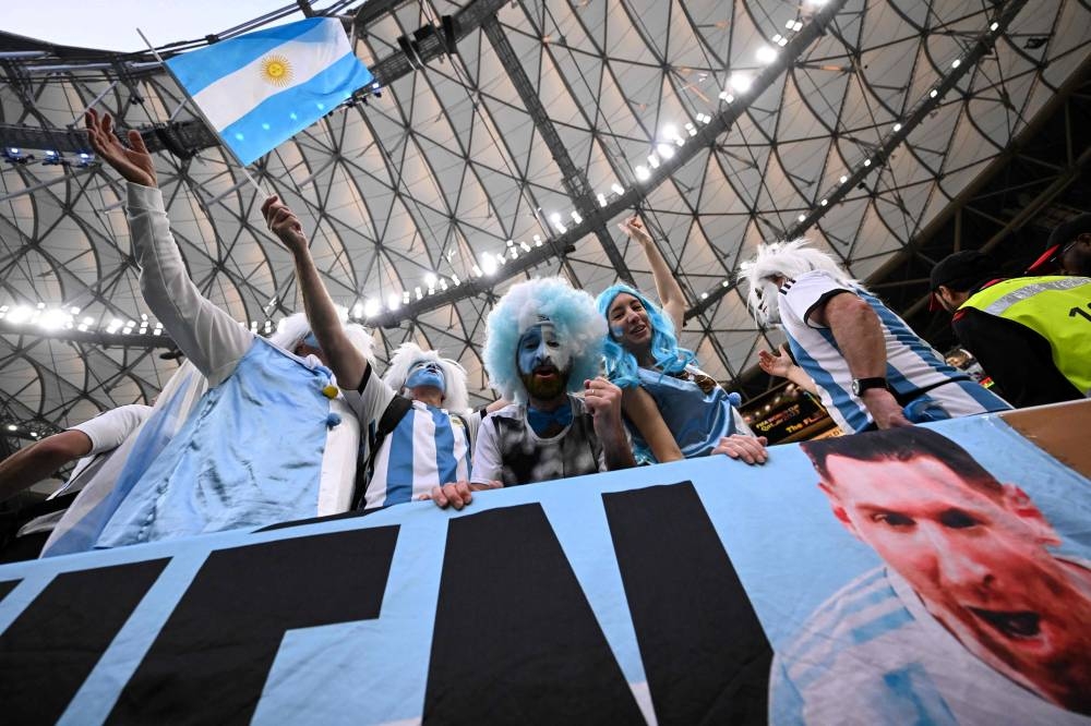 Argentina supporters stand behing a banner depicting Argentina's forward #10 Lionel Messi as they cheer on the stands ahead of the Qatar 2022 World Cup final football match between Argentina and France at Lusail Stadium in Lusail, north of Doha on December 18, 2022. — AFP pic