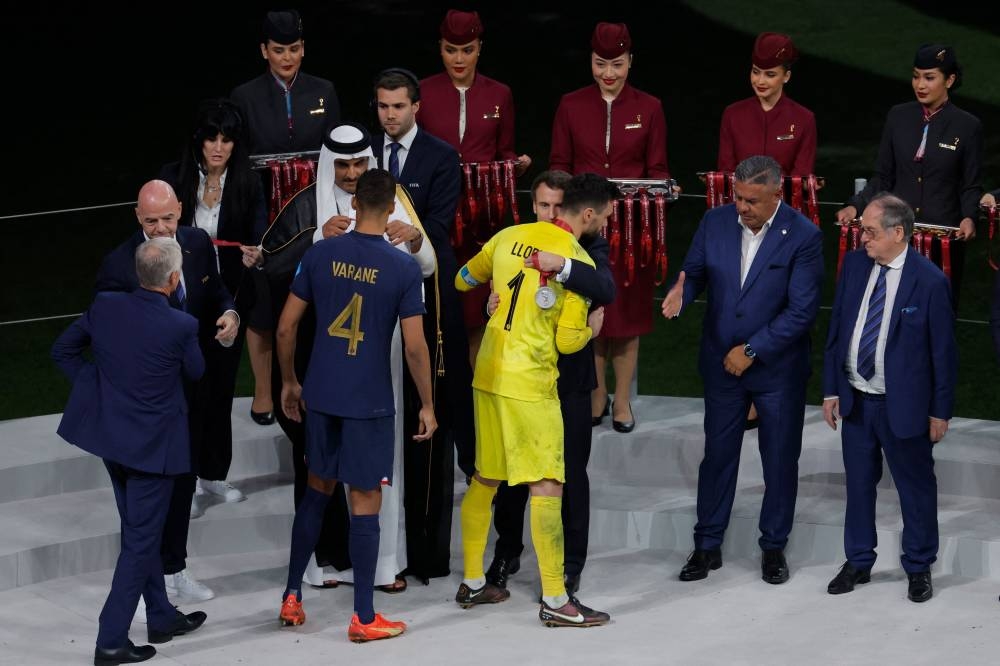 France's goalkeeper #01 Hugo Lloris (centre) is greeted by French President Emmanuel Macron as France's defender #04 Raphael Varane receives his silver medal from the Qatar's Emir Sheikh Tamim bin Hamad al-Thani during the Qatar 2022 World Cup trophy ceremony after losing the football final match between Argentina and France at Lusail Stadium in Lusail, north of Doha on December 18, 2022. — AFP pic