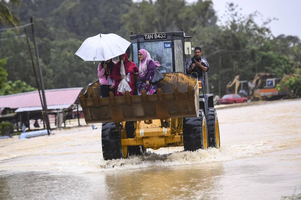 People hitch a ride on an excavator amid heavy rain in Kuala Berang December 10, 2022. — Bernama pic