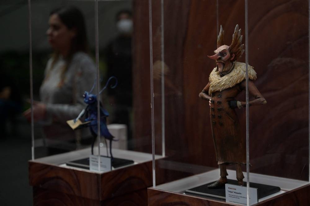 A woman is seen next to statuettes of the characters from the movie Pinocchio by Mexican director Guillermo del Toro exhibited at the Cineteca Nacional , in Mexico City, on December 16, 2022. — AFP pic