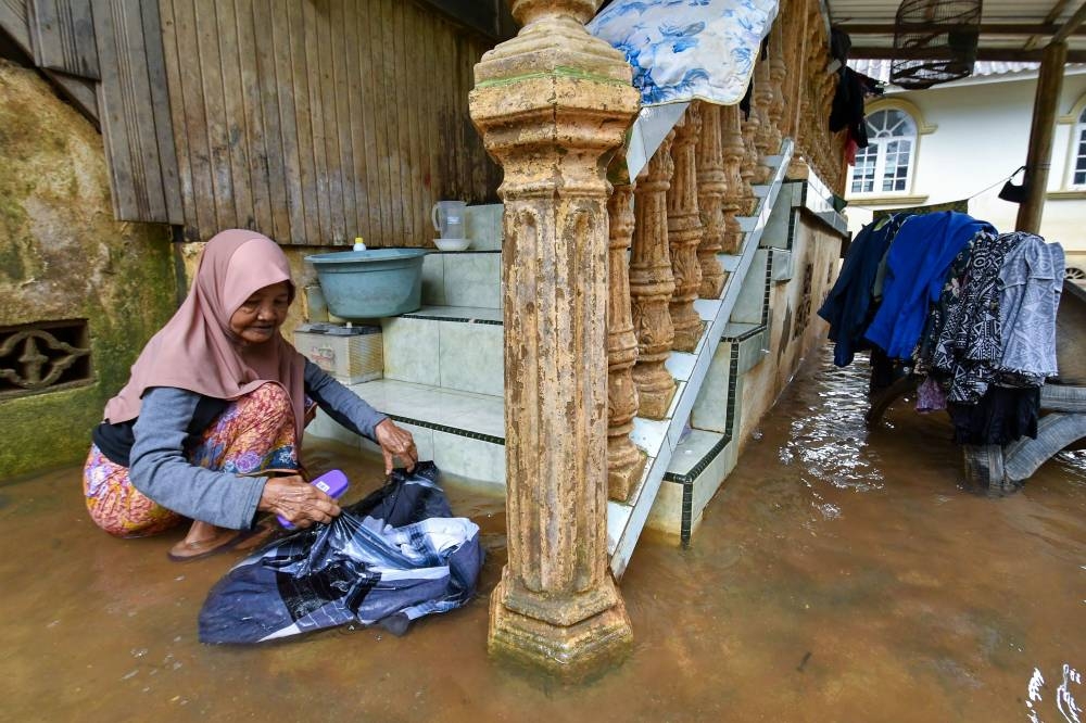 A woman washes clothes outside her flood-hit home in Paris Mas December 26, 2022. — Bernama pic