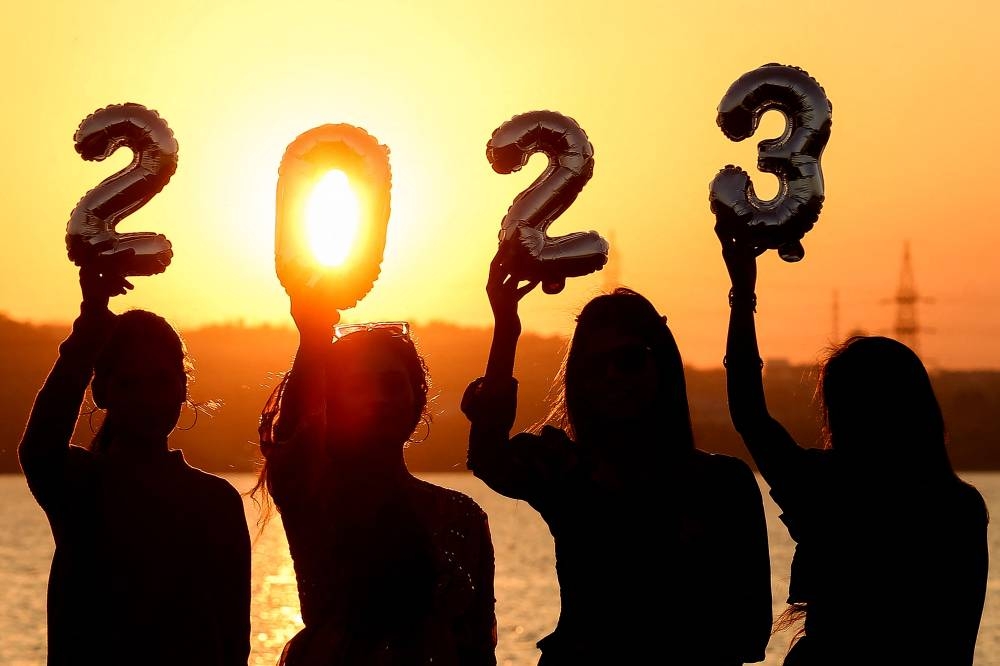 Women are silhouetted against the setting sun as they hold up numeric shaped balloons on the eve of New Year on December 2022. — AFP pic