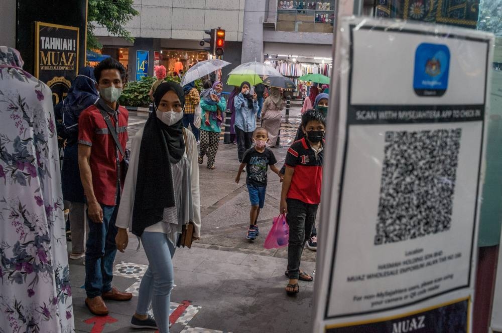 People pass by the QR code of the MySejahtera at a shop-lot  in Kuala Lumpur May 1, 2022. — Picture by Shafwan Zaidon