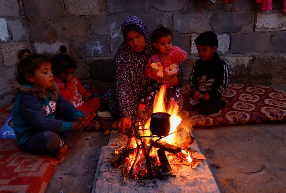 A Palestinian family sits around a wood fire inside their house in Khan Younis in the southern Gaza Strip, January 2, 2023. — Reuters pic