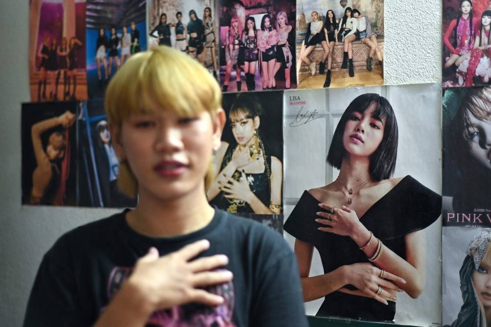 This photograph taken on January 3, 2023 shows posters of popular South Korean girl band Blackpink behind social media influencer Nipattanachai ‘James’ Thepkamdee and Blackpink superfan as he poses for photographs in his bedroom in Bangkok. — AFP pic