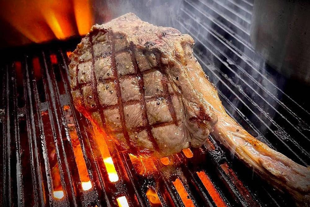 Grilling a tomahawk steak over charcoal.