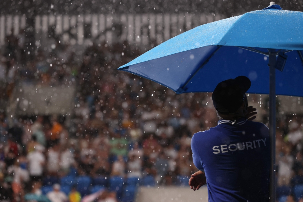 A security member waits behind a umbrella during a suspension due to the rain of the men's singles match between Italy's Fabio Fognini and Australia's Thanasi Kokkinakis on day two of the Australian Open tennis tournament in Melbourne on January 17, 2023. — AFP pic