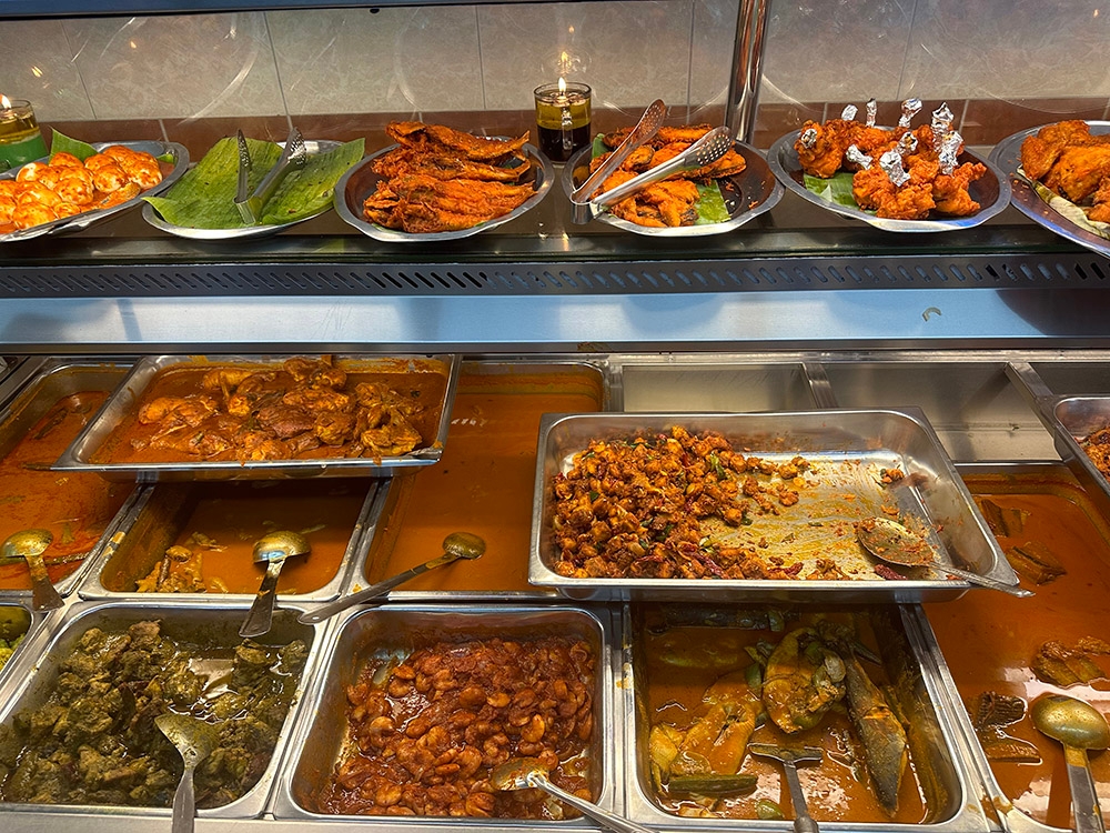 Various curries and deep fried items are laid out at the counter.