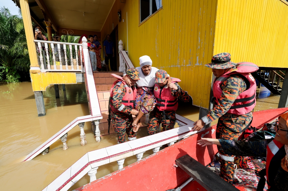 Fire and Rescue Department personnel assist an elderly woman into a boat, in Paitan January 26, 2023. — Bernama pic