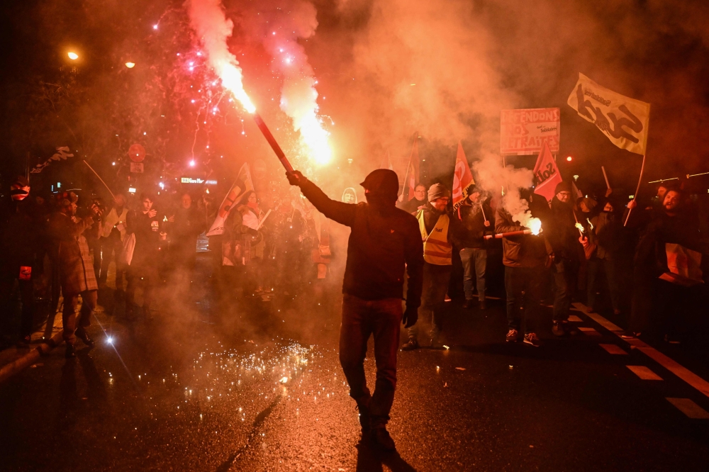 Demonstrators hold flares during a procession against a pension reform in Paris, on January 26, 2023. — AFP pic