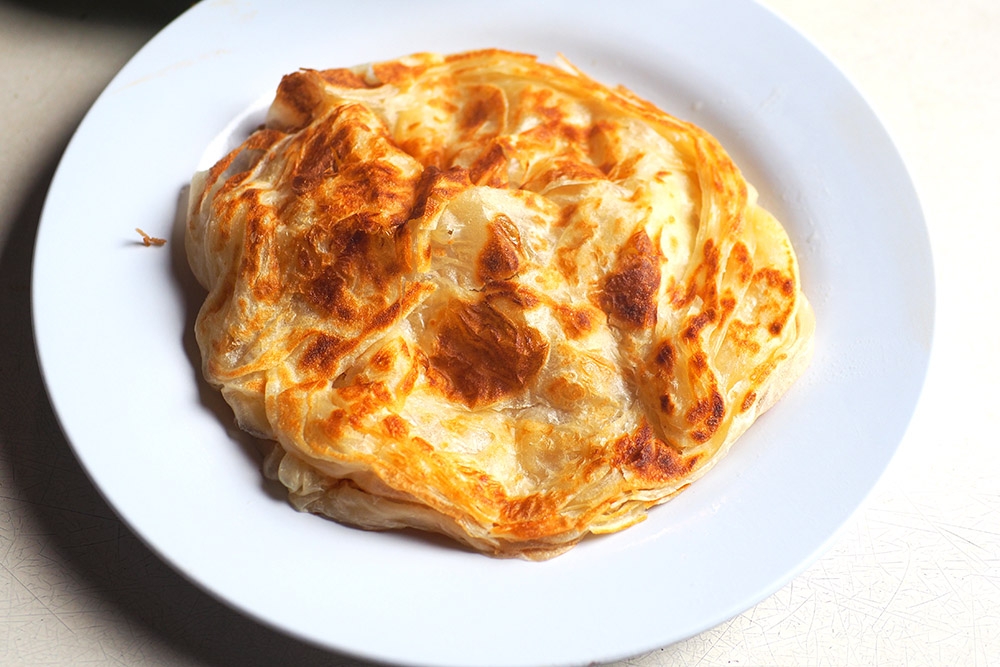 The 'roti canai' has a light, fluffy texture with crispy golden brown bits.