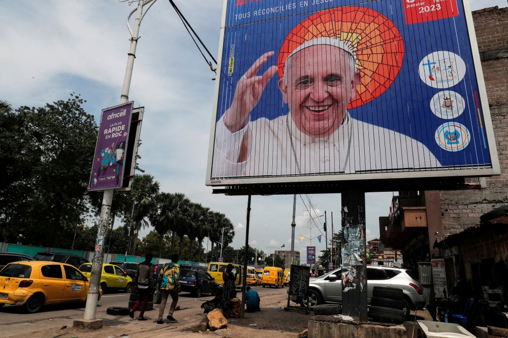 People walk next to the billboard of Pope Francis a day ahead of his arrival in Kinshasa, Democratic Republic of Congo January 30, 2023. ― Reuters pic