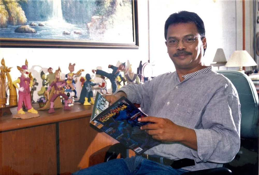 The late Kammaruddin Ismail poses near figurines from his  Keluang Man series while holding a copy of its comic book in this undated photograph. — Picture courtesy of Kamn Ismail’s family