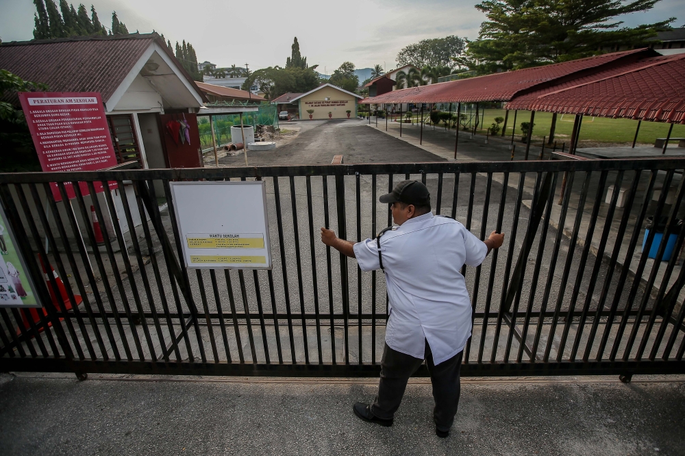 File picture of a security guard from SK Panglima Bukit Gantang Ipoh closing the gate of the school during the movement control order due to the Covid-19 outbreak March 17, 2020. — Picture by Farhan Najib