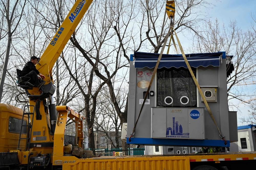 In this picture taken on February 8, 2023, a worker operating a crane moves a nucleic acid testing booth onto a flatbed truck at a park in Beijing. — AFP pic