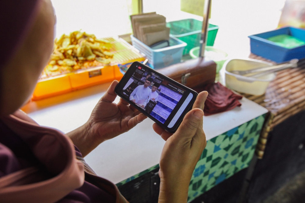 A close up shot of a person using a mobile phone to watch Finance Minister Datuk Seri Anwar Ibrahim tabling the 2023 budget, February 24,2023. — Picture by Ahmad Zamzahuri