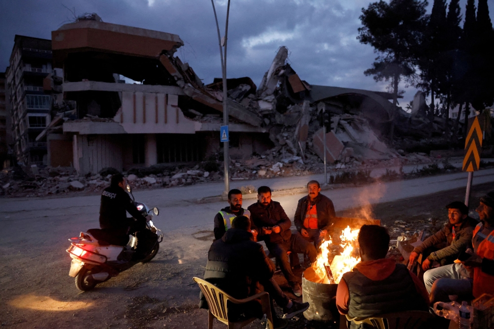 People warm themselves by a fire beside a collapsed building and rubble, in the aftermath of a deadly earthquake, in Antakya, Hatay province, Turkiye, February 21, 2023. — Reuters pic