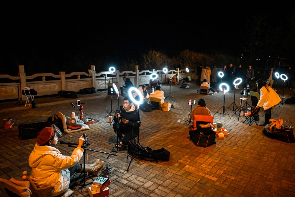 The photo taken on February 20, 2023 shows outdoor livestreamers singing and chatting with the audiences through their mobile phones on an overpass bridge at night in Guilin, in southern China's Guangxi province. — AFP pic