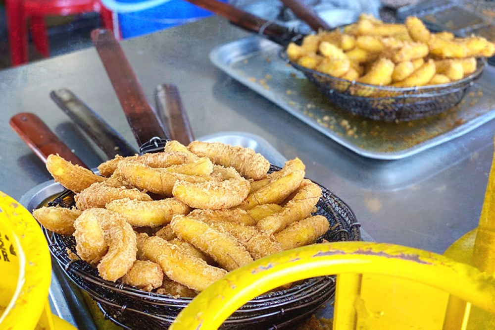 Freshly fried 'goreng pisang' being drained of excess oil with large strainers.