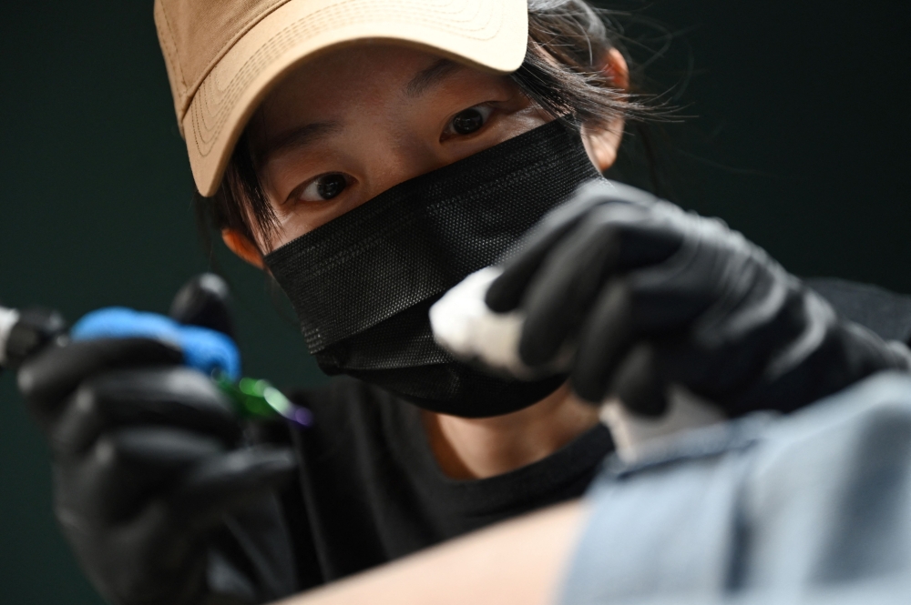 Chinese tattoo artist Song Jiayin tattooing the leg of her client Liao Jingyi at her studio in Beijing. — AFP pic