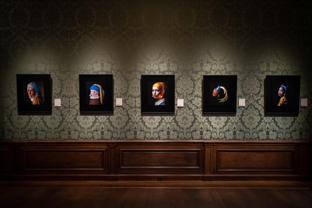 This photograph taken in The Hague on March 9, 2023 shows an image designed with artificial intelligence by Berlin-based digital creator Julian van Dieken (centre) inspired by Johannes Vermeer's painting ‘Girl with a Pearl Earring’ at the Mauritshuis museum. — AFP pic