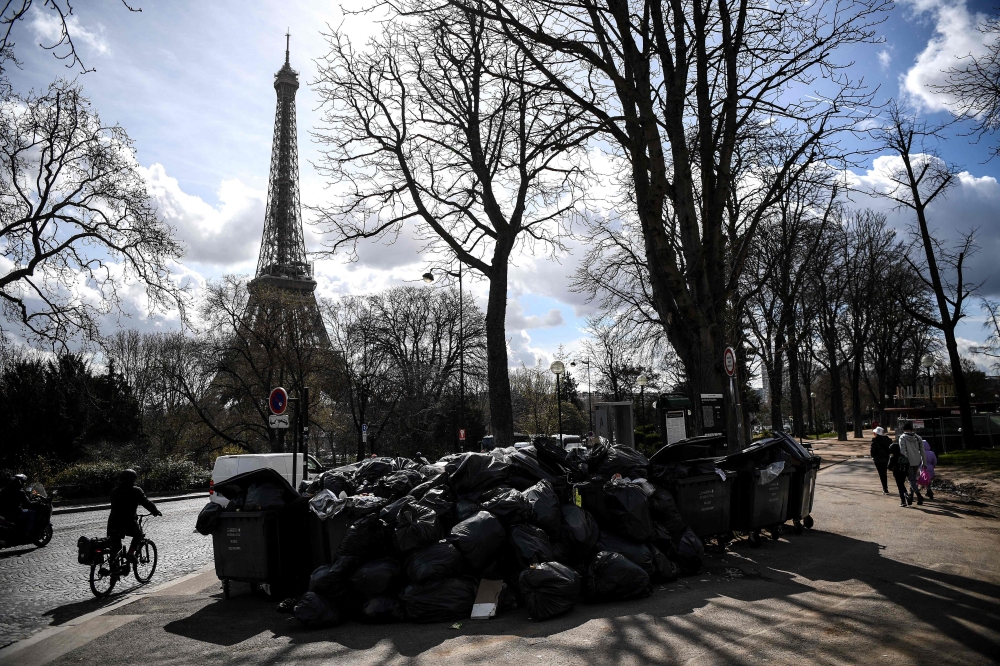 Pedestrians walk past a pile of garbage bags that have been piling up since waste collectors went on strike against the French government's proposed pensions reform, in front of the Eiffel tower in Paris on March 15, 2023. — AFP pic