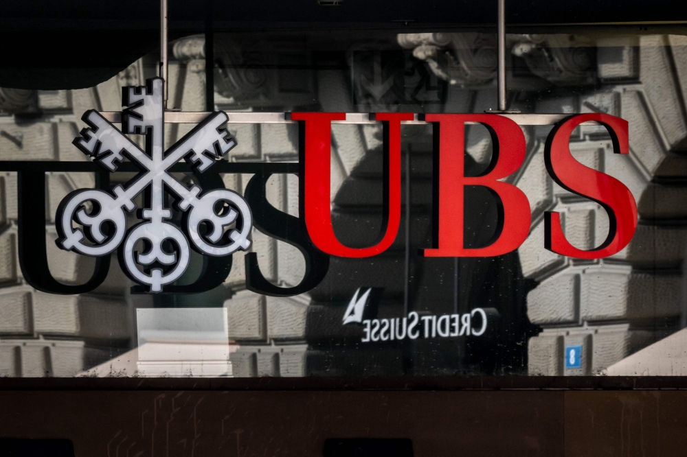 A photograph shows a logo of Swiss giant bank UBS in front of a logo of Credit Suisse bank in Zurich on March 19, 2023. — AFP pic