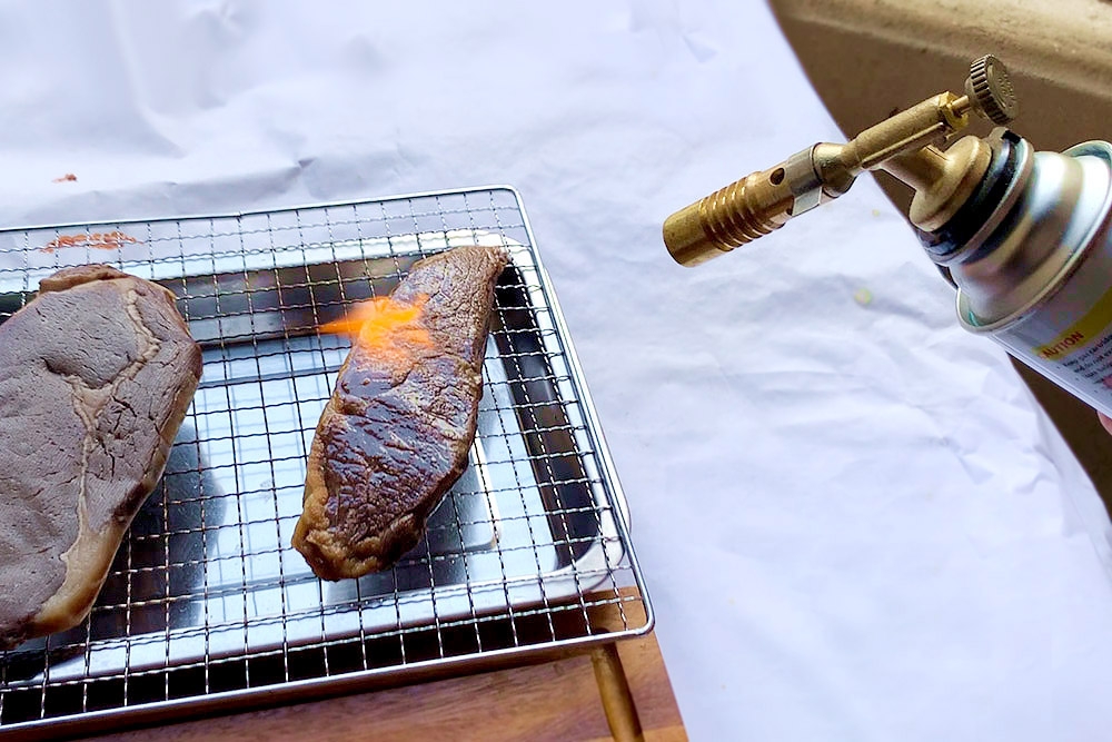 Searing the steaks using a culinary butane torch.