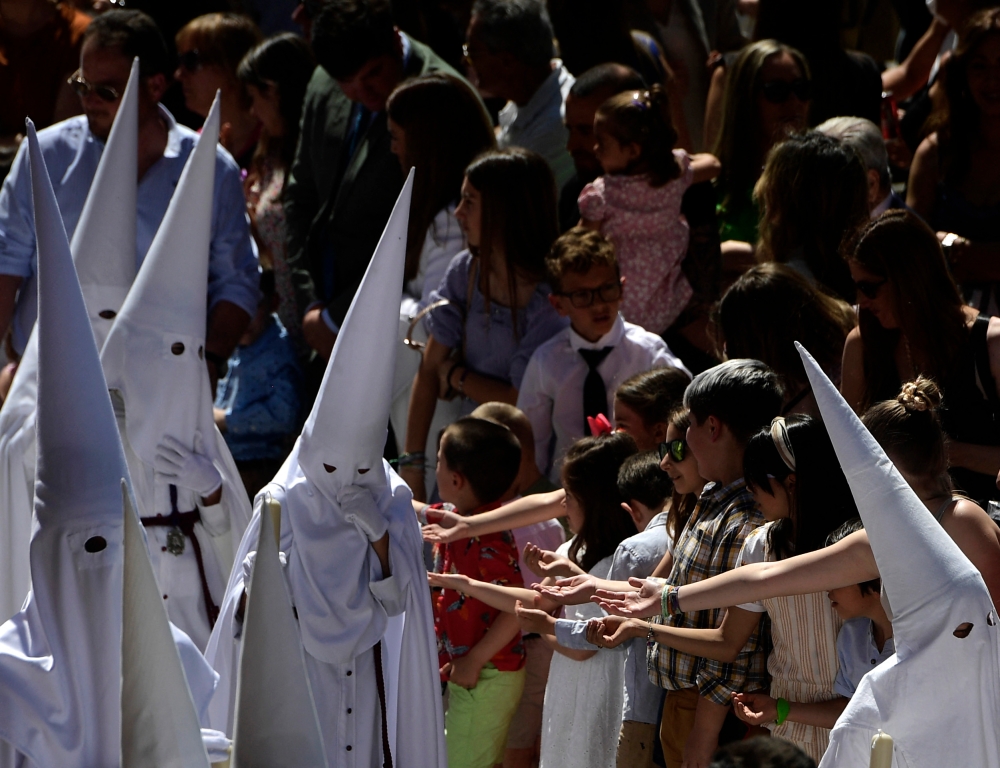 Children ask for candies to the penitents of La Paz brotherhood during the Palm Sunday procession in Seville on April 2, 2023. — AFP pic
