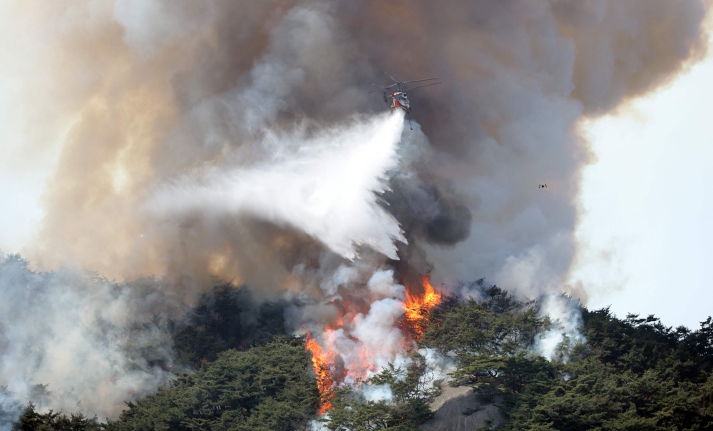 This picture taken on April 2, 2023 shows a helicopter dousing a wildfire on Mount Inwang in Seoul. — Yonhap/AFP pic