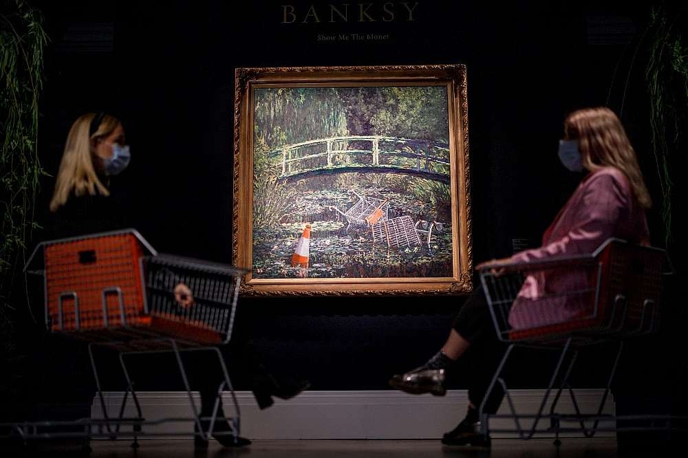 Assistants by an artwork entitled 'Show me the Monet' by British street artist Banksy at Sotheby's Galleries in central London October 16, 2020. — AFP pic
