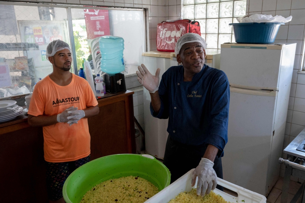 Brazilian chef Carlos Alberto da Silva (right), known as Nego Breu, speaks while cooking food to be delivered to the homeless population of the city center of Rio de Janeiro at the restaurant Chapeu do Chef, at the Chapeu Mangueira favela in Rio de Janeiro, Brazil, on March 9, 2023. — AFP pic