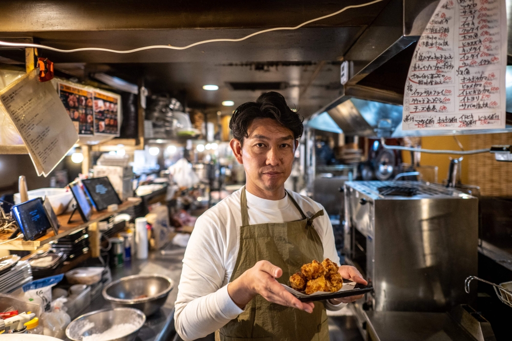 This picture taken on March 14, 2023 shows Takehiro Matsumoto posing with a plate of cooked karaage at an izakaya bar in the Kamata district of Tokyo. — AFP pic
