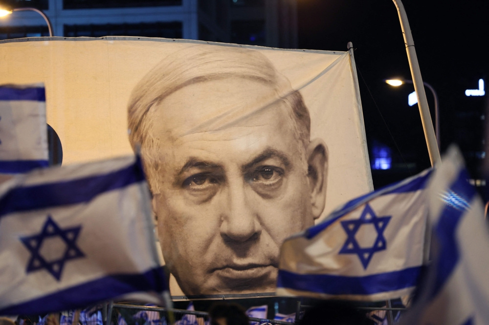 Demonstrators wave flags next to a banner depicting Israeli Prime Minister Benjamin Netanyahu during a rally to protest the government's judicial overhaul bill in Tel Aviv April 22, 2023. — AFP pic