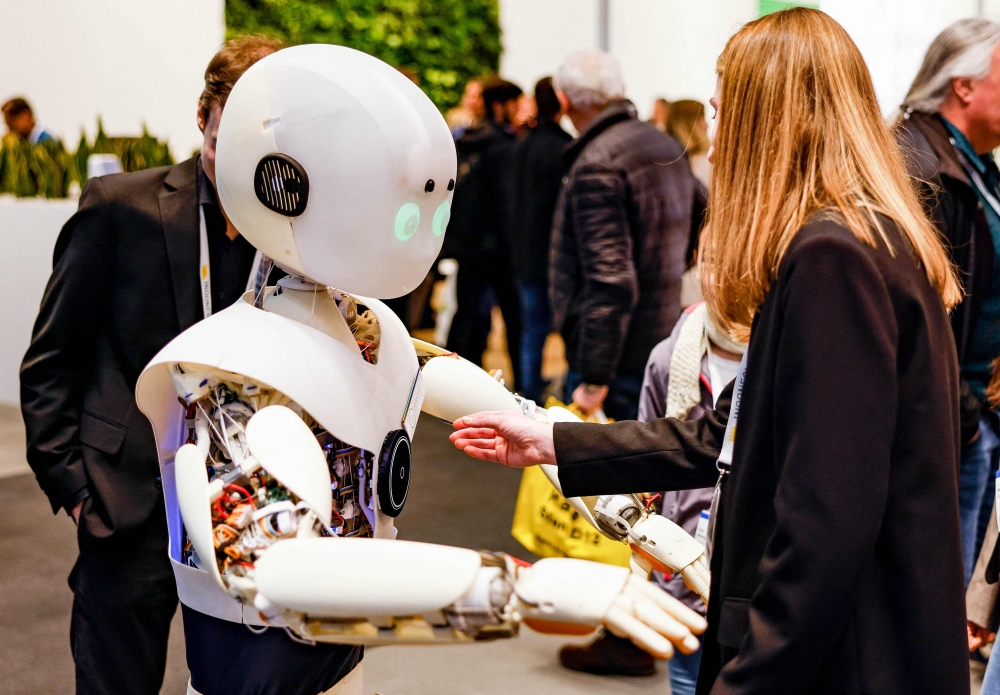 In this file photo taken on April 17, 2023 a woman interacts with a robot by Devanthro — The Robody Company in front of a photo box at the Hannover Messe 2023, the Hanover technology fair, in Hanover. — AFP pic