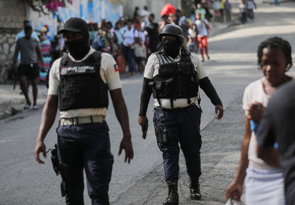 Police officers walk near people who carry their belongings while fleeing their homes and neighbourhood due to clashes between gangs, in Port-au-Prince, Haiti April 24, 2023. — Reuters pic