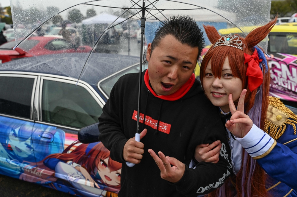 Car owner Yosuke Takahata posing in front of his car with a woman dressed up as anime character Daiwa Scarlet. — AFP pic