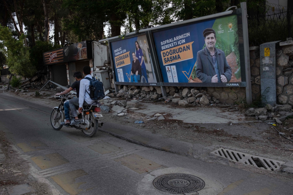 Two men ride a motorcycle past election campaign posters of Turkey’s Justice and Development Party (AKP) in Hatay, a city which suffered the most damage in the earthquakes that occurred in southern Turkey, on May 12, 2023. — AFP pic