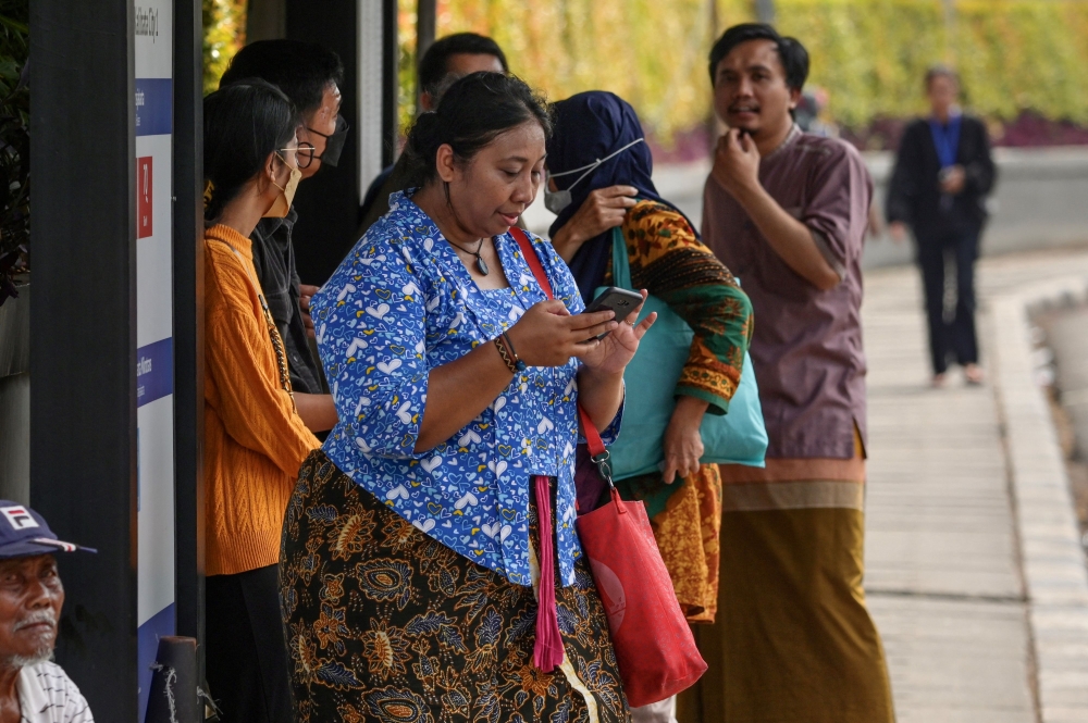 Telly Nathalia (centre), wearing a traditional kebaya, waits for public transport in Jakarta April 15, 2023. — AFP pic