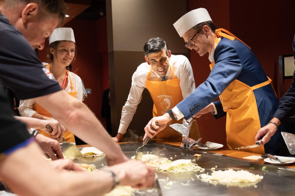 Britain's Prime Minister Rishi Sunak (2nd right) is shown how to make traditional Japanese Okonomiyaki pancakes at a restaurant in Hiroshima with travelling British journalists including BBC Political Editor, Chris Mason (right), on the sidelines of the G7 Summit Leaders' Meeting May 20, 2023. — Stefan Rousseau/Pool/AFP pic