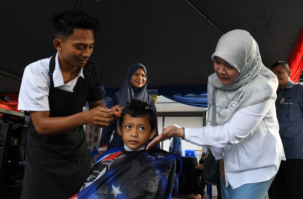 Education Minister Fadhlina Sidek (right) watches as Mohamad Ali Azuan, 7, gets an RM3 haircut at the Seberang Perai Selatan district-level Kita Madani Carnival in Sungai Duri, Nibong Tebal May 27, 2023. — Bernama pic