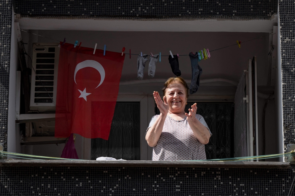 A woman applauds from her house to supporters of Turkey’s opposition presidential candidate Kemal Kilicdaroglu, walking on the streets to persuade people to vote for him, in Istanbul on May 23, 2023. — AFP pic